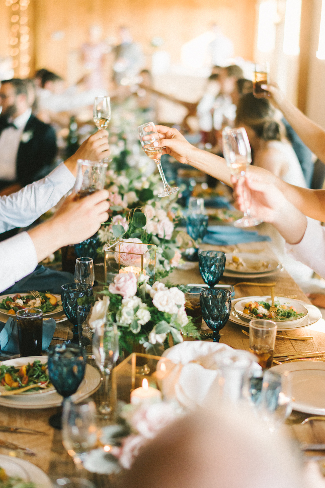 Guests at an indoor reception at a Shadow Creek wedding do a toast with their glasses over a long table