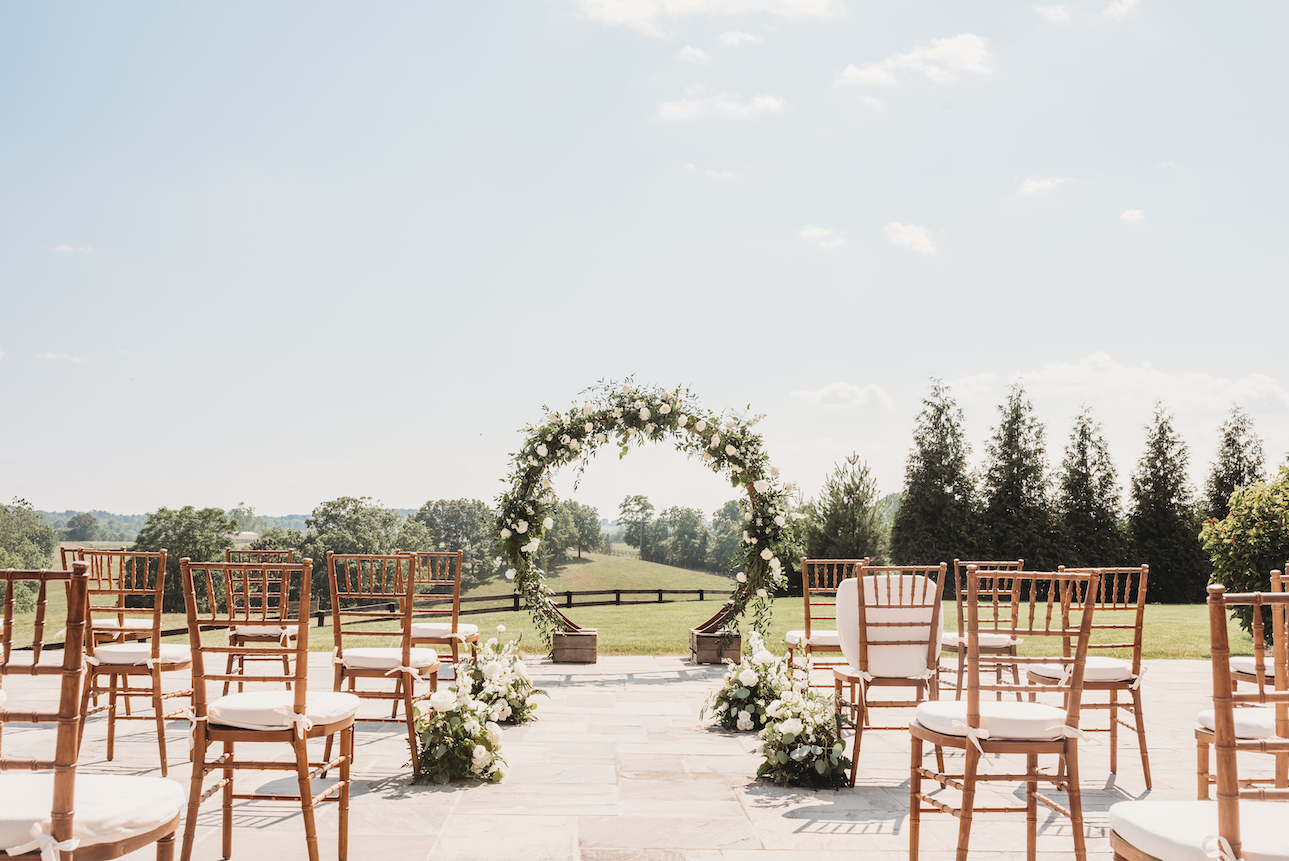 A circle arch floral installation stands at the front of an outdoor wedding ceremony space