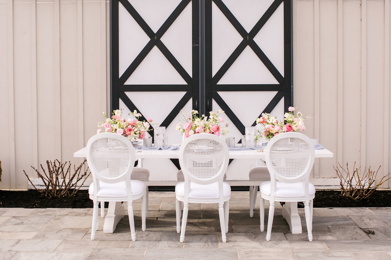 A white table and chairs with three pink floral centerpieces