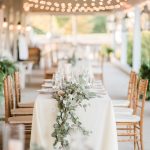 Light greenery flows over a long table sitting outside under the patio at Shadow Creek wedding venue in Virginia