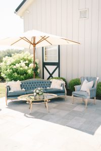 An antique blue couch and a matching chair sits under a white umbrella outside of Shadow Creek Barn wedding venue